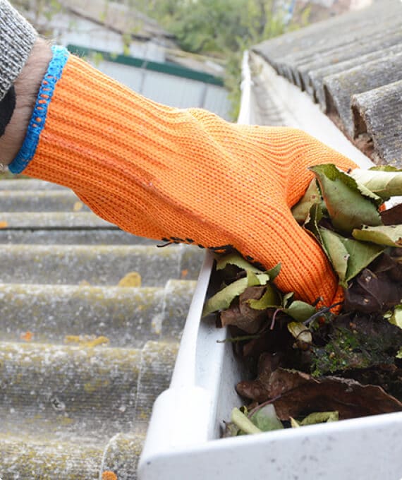 Gloved hand cleaning leaves out of gutter